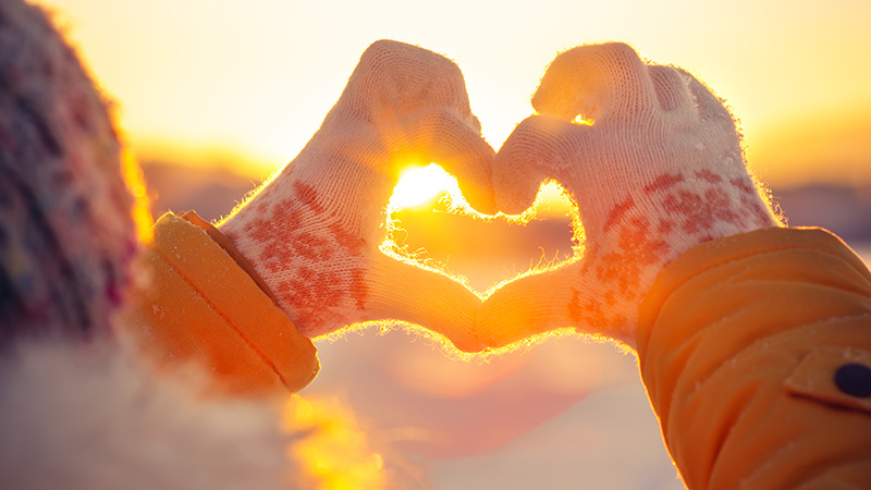 Woman hands in winter gloves Heart symbol shaped Lifestyle and Feelings concept with sunset light nature on background