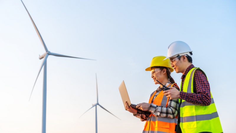 Young,Engineer,Team,Working,With,Laptop,Computer,Against,Wind,Turbine