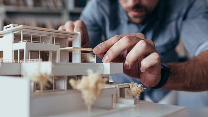 Close,Up,Of,Male,Architect,Hands,Making,Model,House.,Man