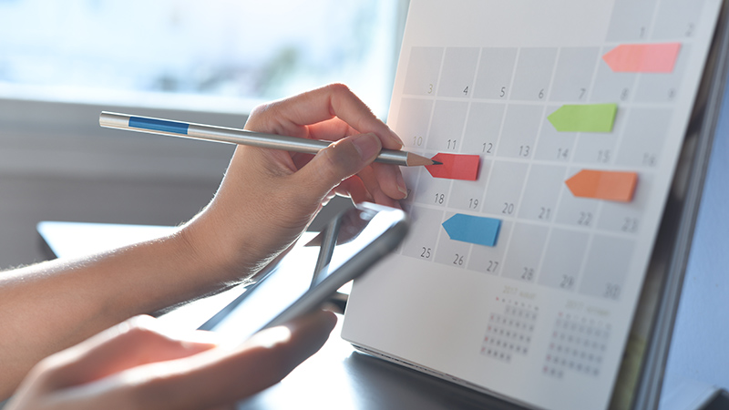 2024 Event planner timetable agenda plan on schedule event. Business woman checking planner on mobile phone, taking note on calendar desk on office table. Calendar event plan, work planning