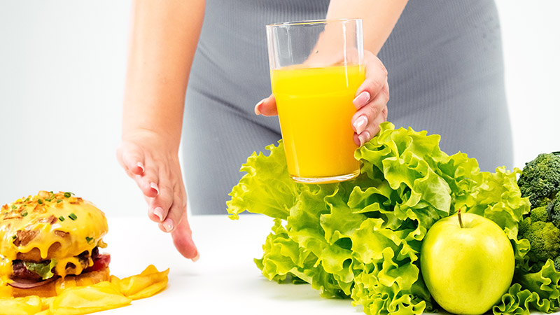 Persona eligiendo alimentos saludables sobre comida chatarra con jugo natural y vegetales frescos