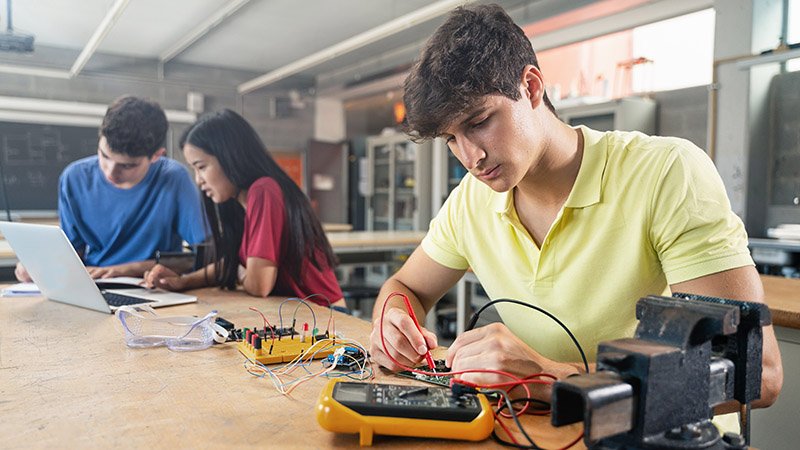 Estudiantes de ingeniería electrónica realizando práctica de circuitos en laboratorio universitario